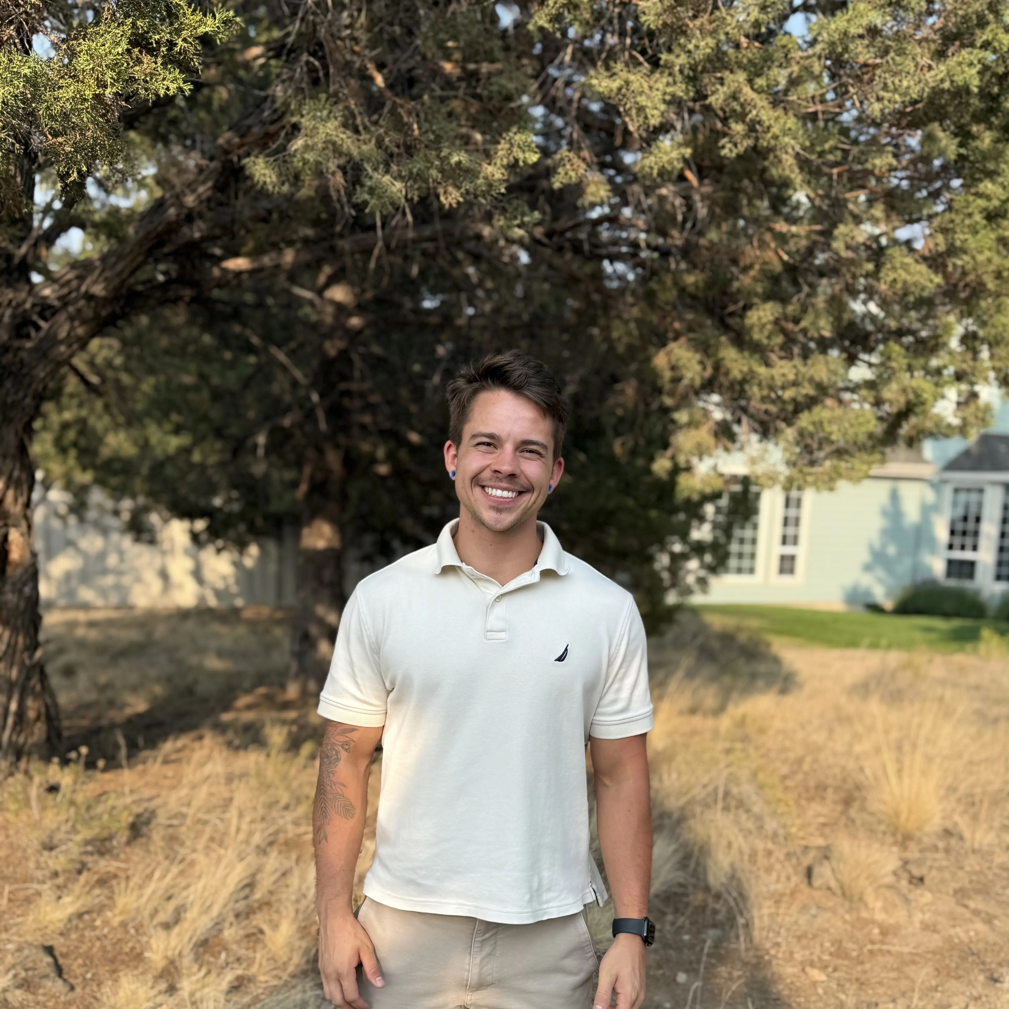 Castle Ford, founder of Keep Estate Care, outdoors beside a juniper tree.